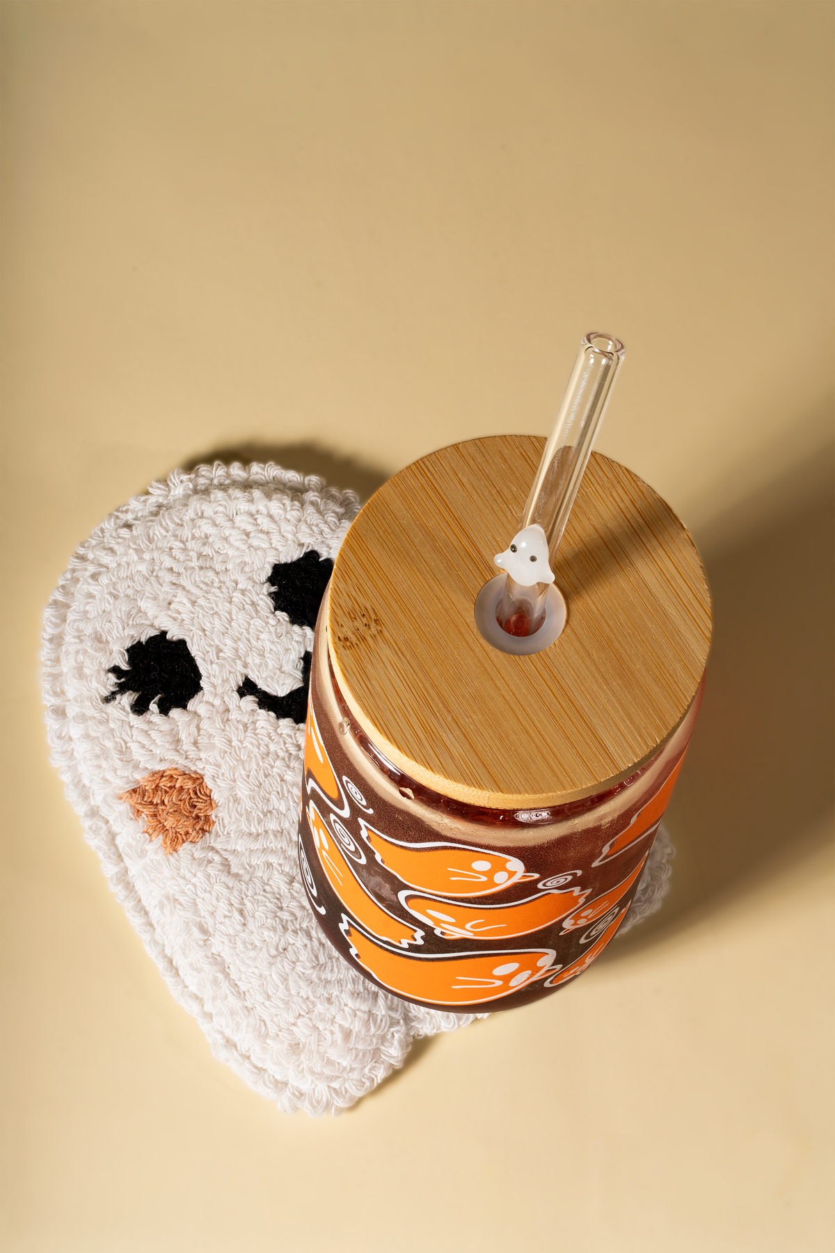 Overhead view of the orange ghost tumbler's bamboo lid and ghost-charm glass straw resting on a tufted ghost-shaped coaster.
