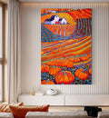 A colorful vertical wall art print depicting a stylized autumn farm scene with orange pumpkins, a white farmhouse, and blue sky, displayed on a white slatted wall above a console table in a modern living room.